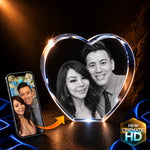 A heart-shaped custom photo display showing a black-and-white portrait of a couple, with a smartphone on the left displaying the same photo and an orange arrow pointing toward the display. The scene is set on a dark draped surface with blue fabric and a gold 'New Cinematic HD' badge in the corner.